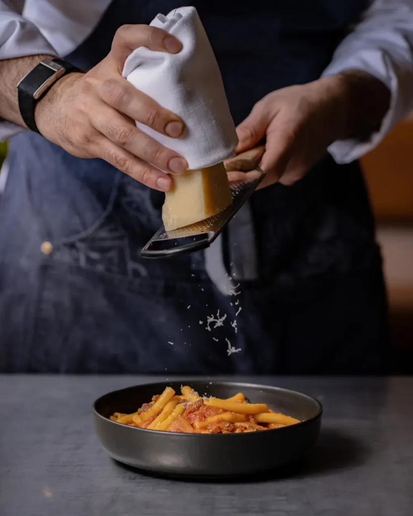 Chef grating Parmesan cheese over a pasta dish
