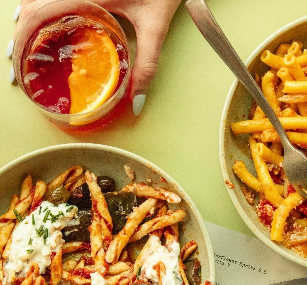 Hand holding a spritz, Strozzapreti and ziti on green table