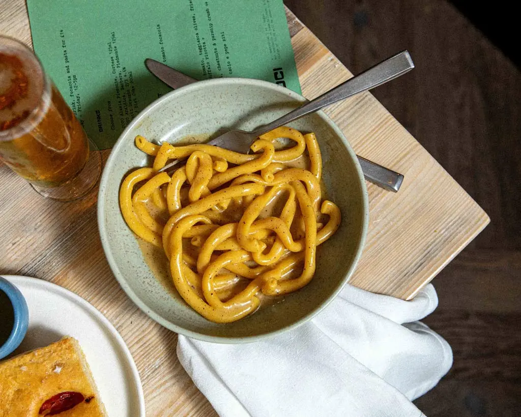 Top down view of brown butter cacio e pepe ziti, focaccia and a beer
